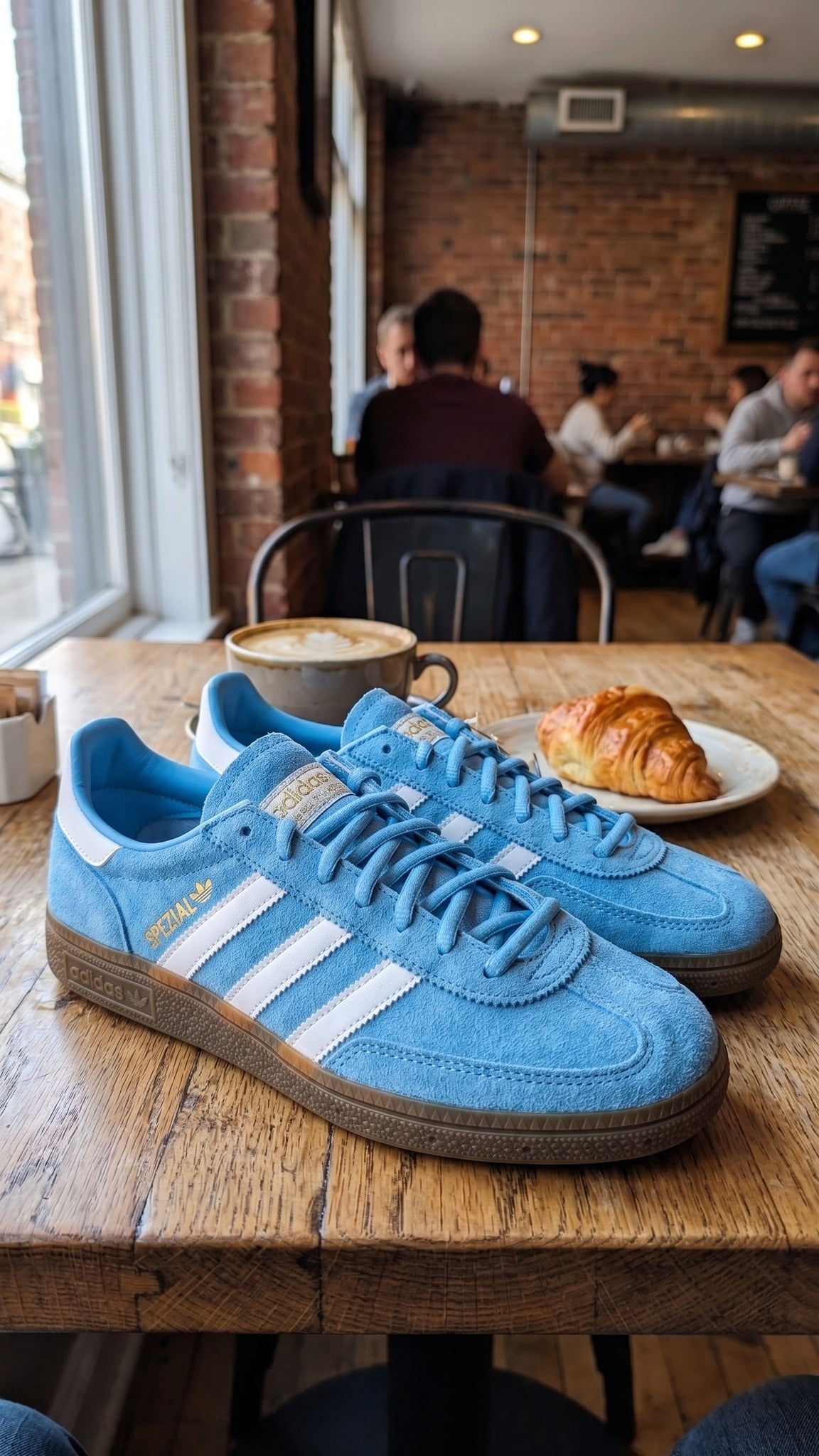 A pair of the blue sneakers on a wooden cafe table next to a cup of coffee.