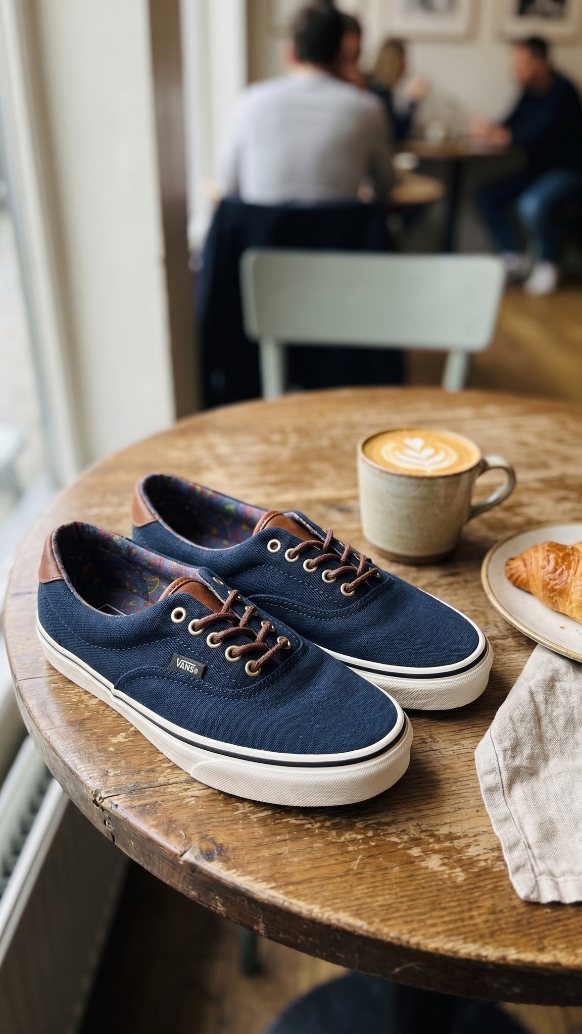 Two shoes sitting on a wooden cafe table next to a coffee cup.