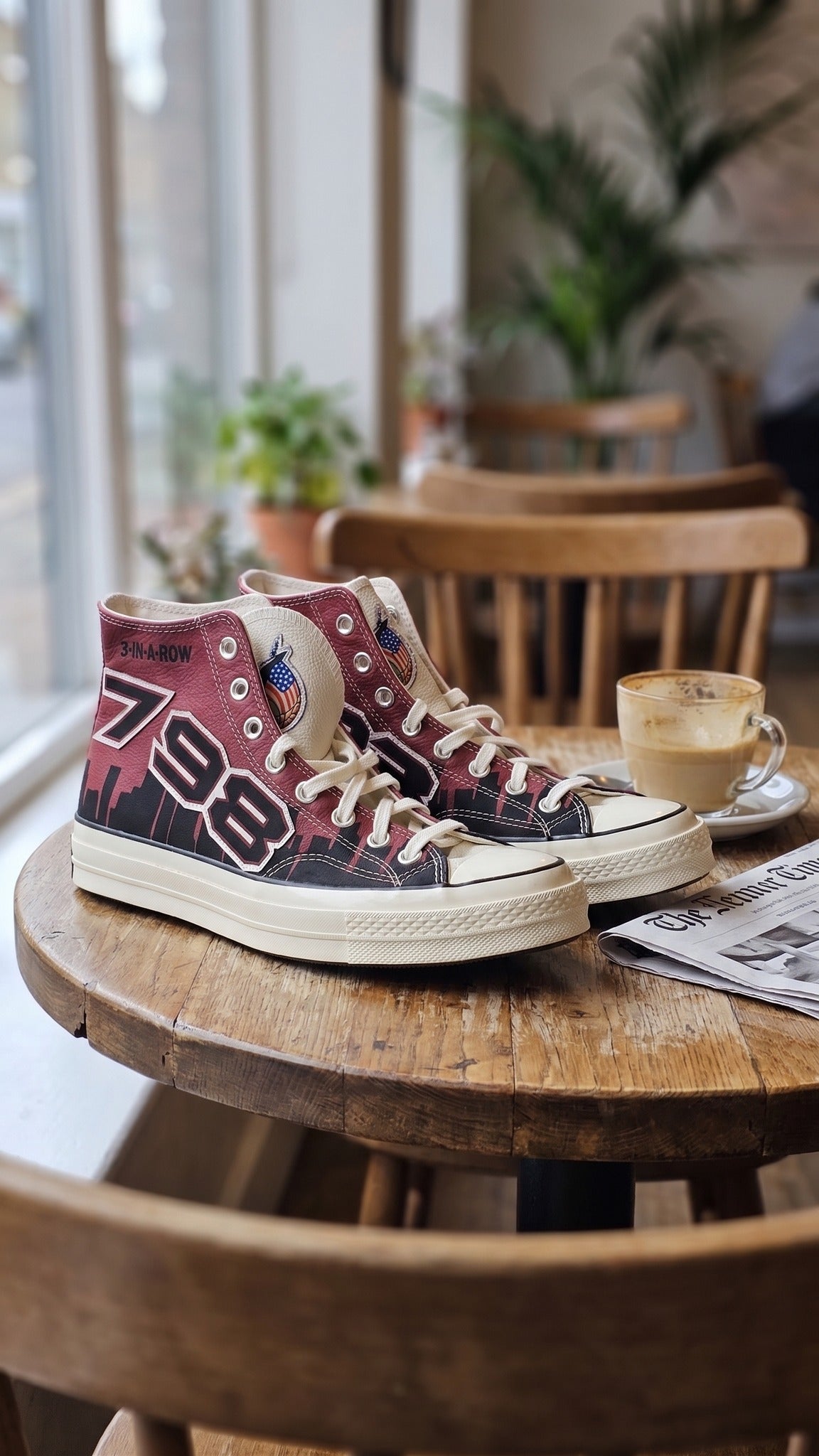 Both sneakers displayed on a wooden round table next to a coffee cup.