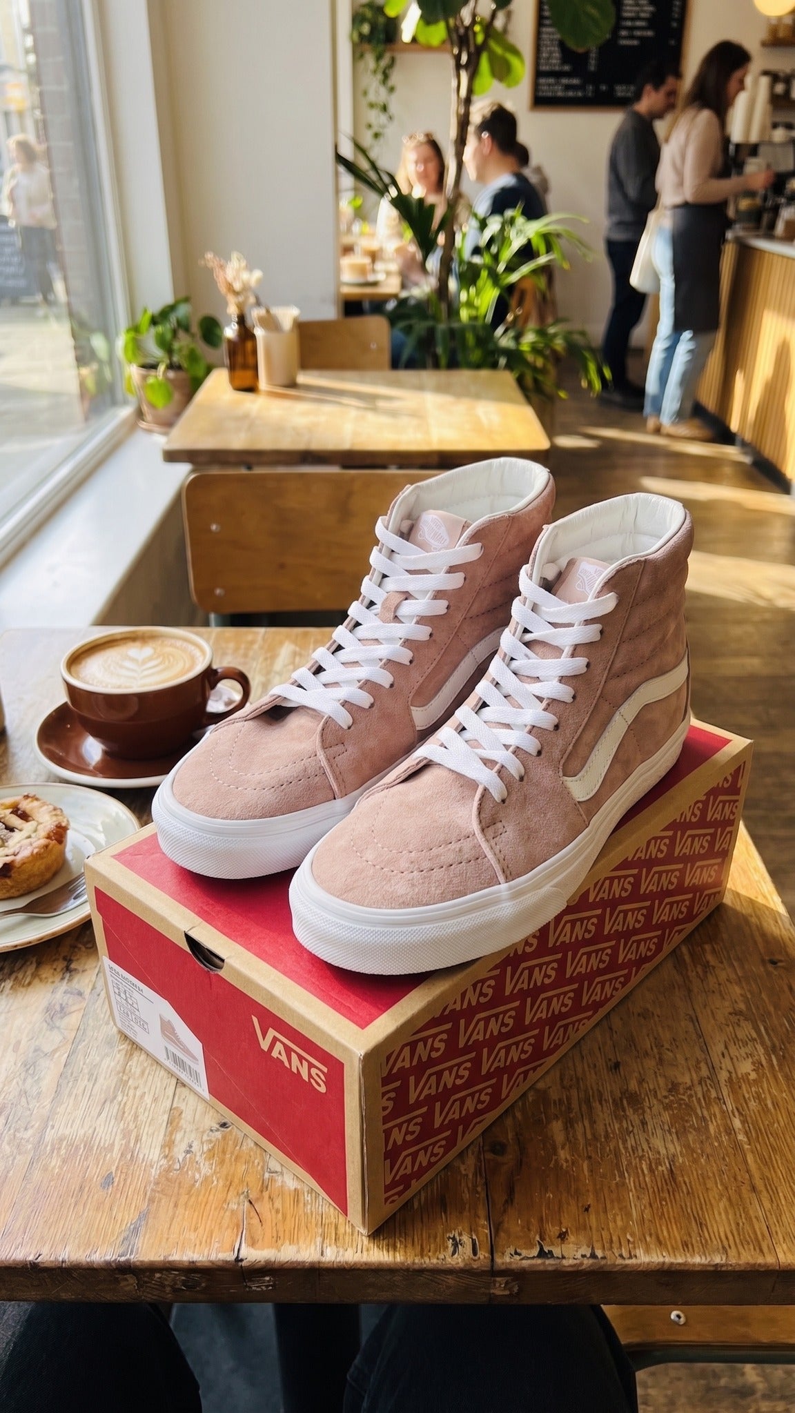 Three-quarter lifestyle view of both shoes on the red box, set on a cafe table.