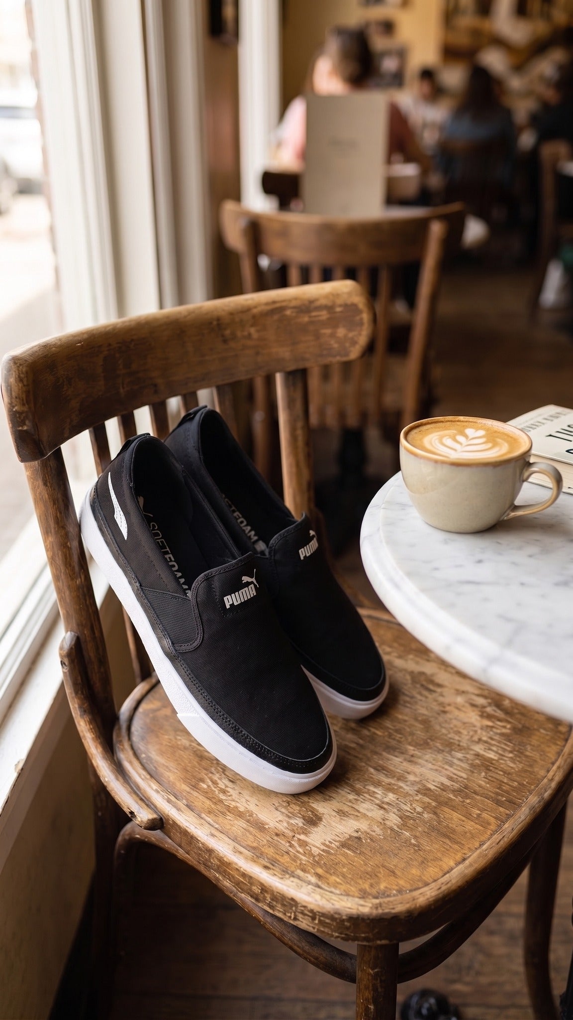 Lifestyle view of the shoes resting on a wooden chair in a cafe next to a coffee cup.
